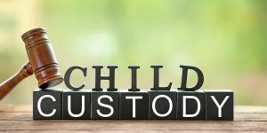 Text CHILD CUSTODY made of black blocks and letters with judge gavel on table against blurred background, closeup