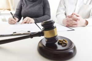 Judges gavel on table with wedding rings and people in the background